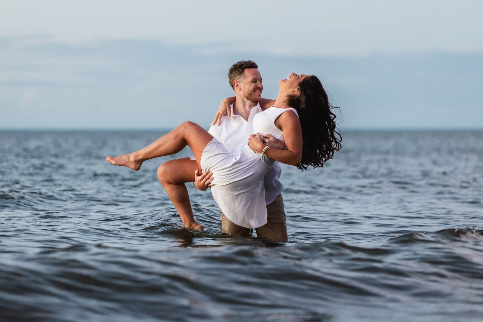 Sheldon lifting Danielle as she laughs, both wading in the water at dusk